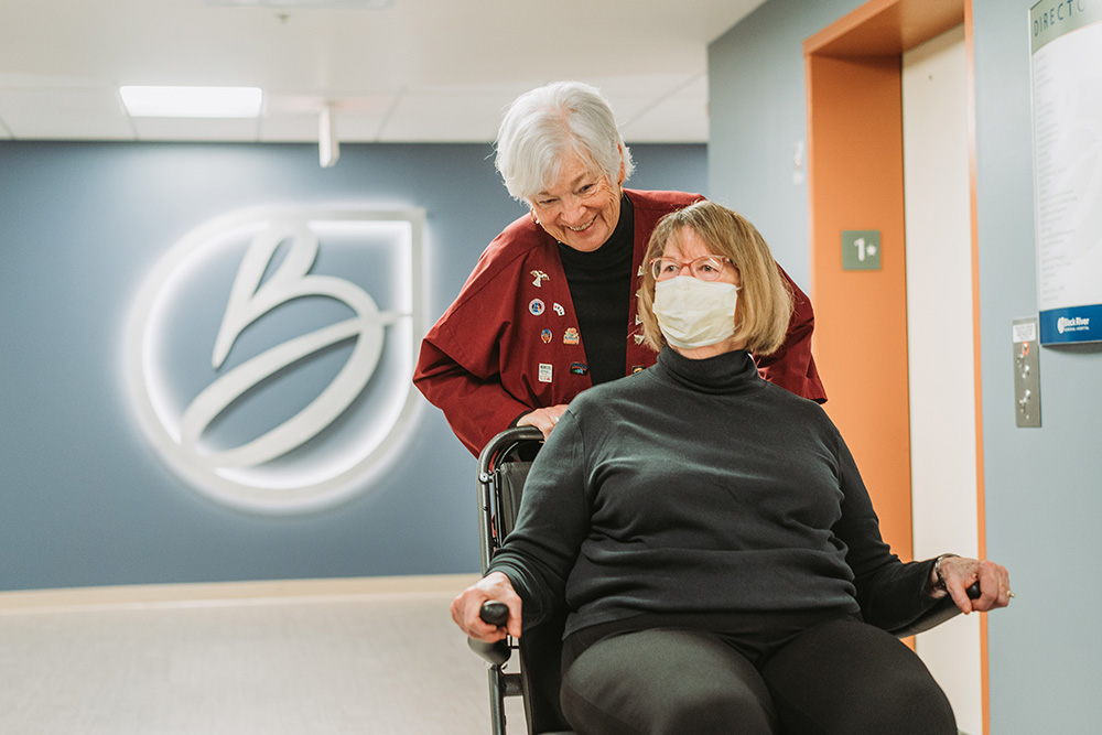 A Black River Memorial Hospital volunteer pushes a woman in a wheelchair through a hallway